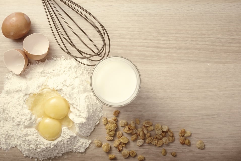 Ingredients and tools to make a cake, flour, milk, raisin ,eggs. With space for text.