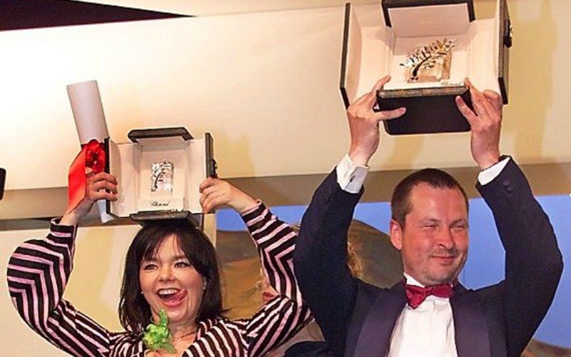 Lars Von Trier and Bjork are holding up Golden Palm 2000 trophies over their heads.