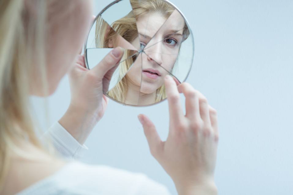 Young woman touching her own reflection in a broken mirror Young woman touching her own reflection in a broken mirror
