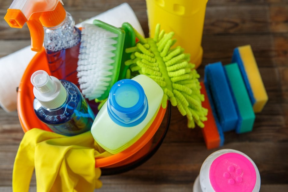 Plastic bucket with cleaning products on wooden background