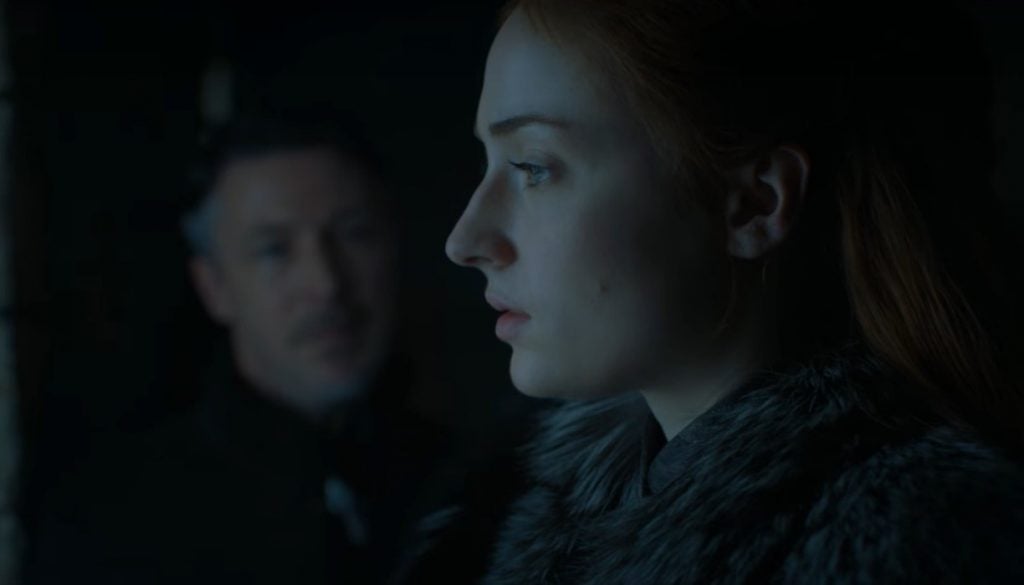 Sansa in the foreground, looking pensively to the left of the frame, with Littlefinger advising her from the shadows in the background