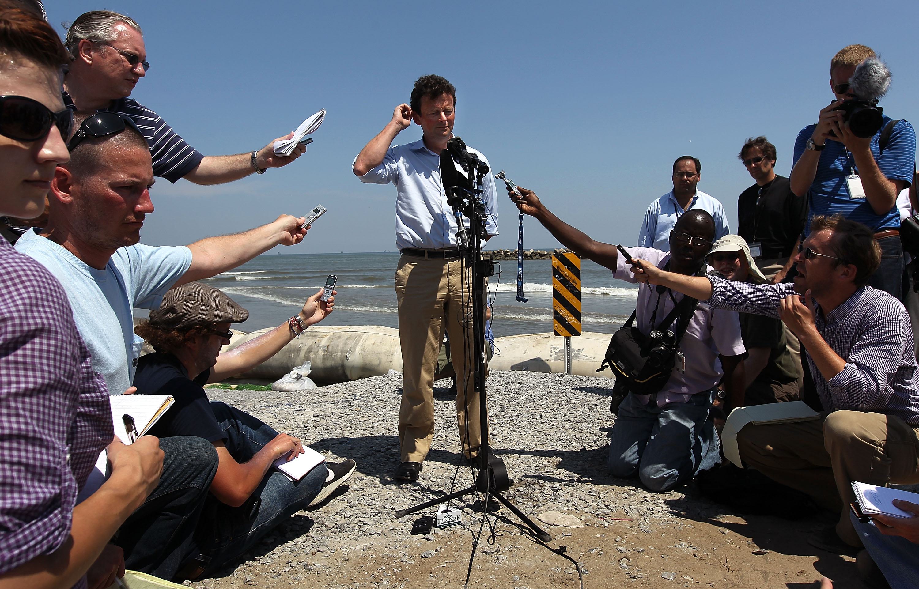Former BP CEO Tony Hayward answers questions from the media on an oil-stained beach.