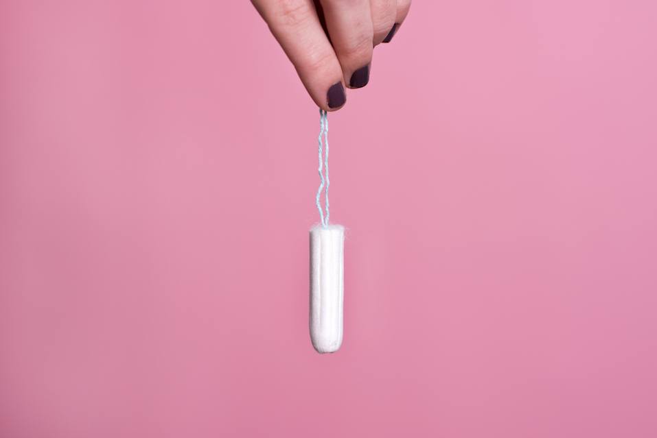 Woman's hand holding a clean cotton tampon in a pink background