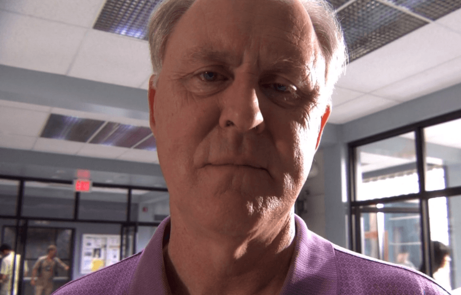 John Lithgow wearing a purple shirt, staring menacingly into the camera