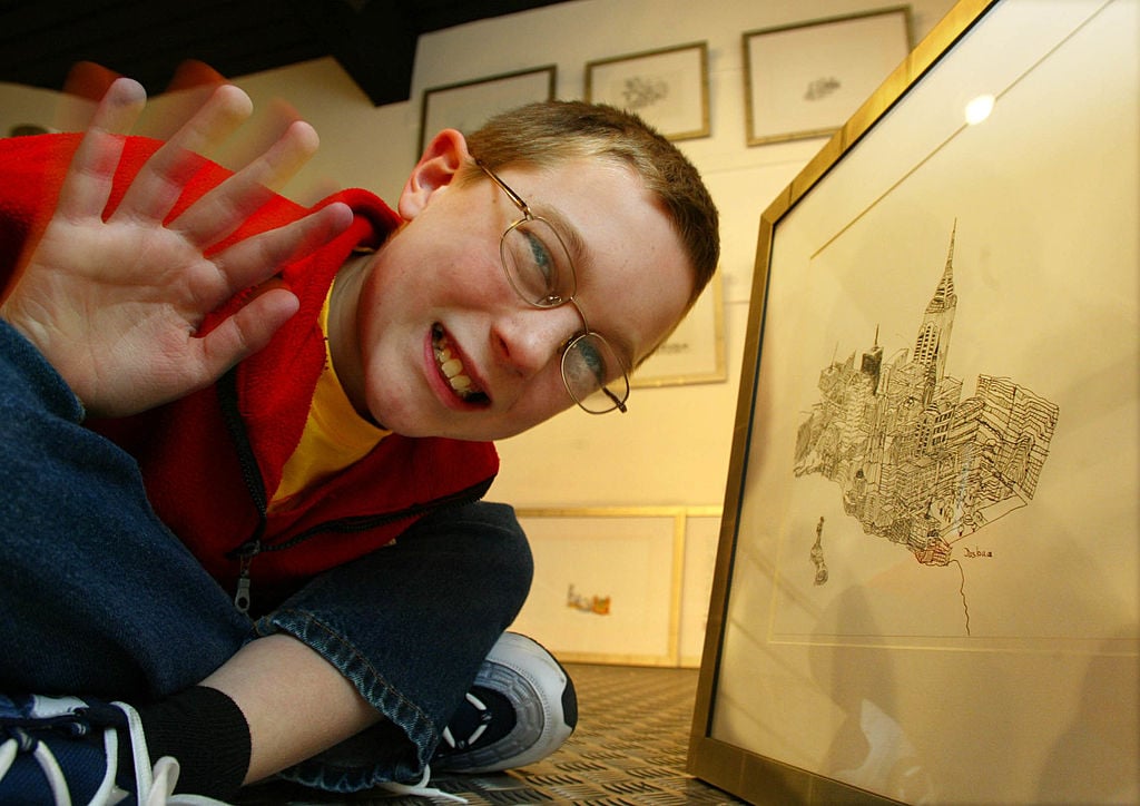 A young man with autism poses among his drawings