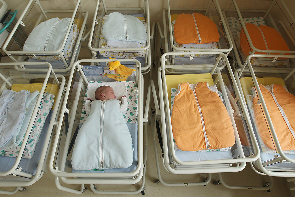 A newborn baby lies in a baby bed in the maternity ward of a hospital
