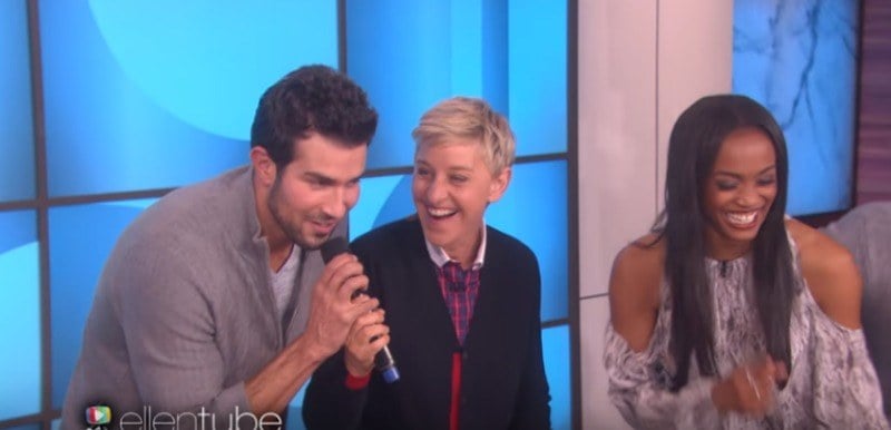 Bryan is taking the microphone from Ellen DeGeneres and Rachel Lindsay is laughing.