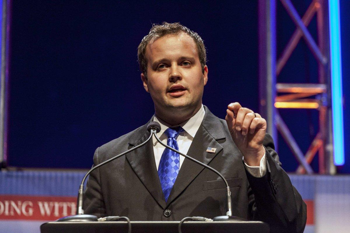Josh Duggar wearing a suit, and speaking into a microphone while pointing