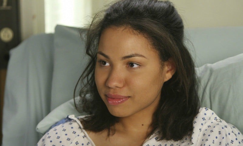 Jurnee Smollett-Bell is sitting up in a hospital bed in a hospital gown.