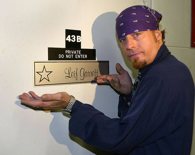 Leif Garrett in a purple bandana gestures to a star name plaque on his dressing room.