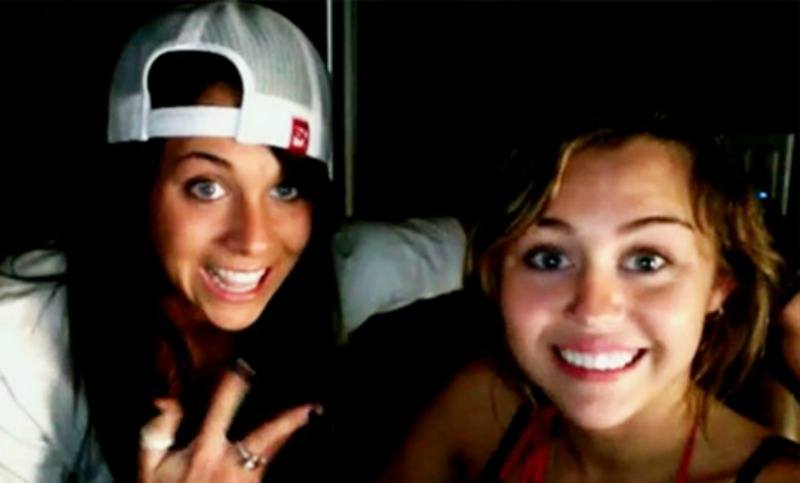 Mandy Jiroux is wearing a backwards cap and is posing next to a smiling Miley Cyrus.