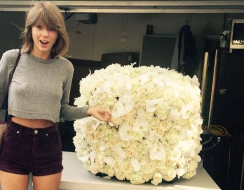 Taylor Swift points to a cube of white flowers