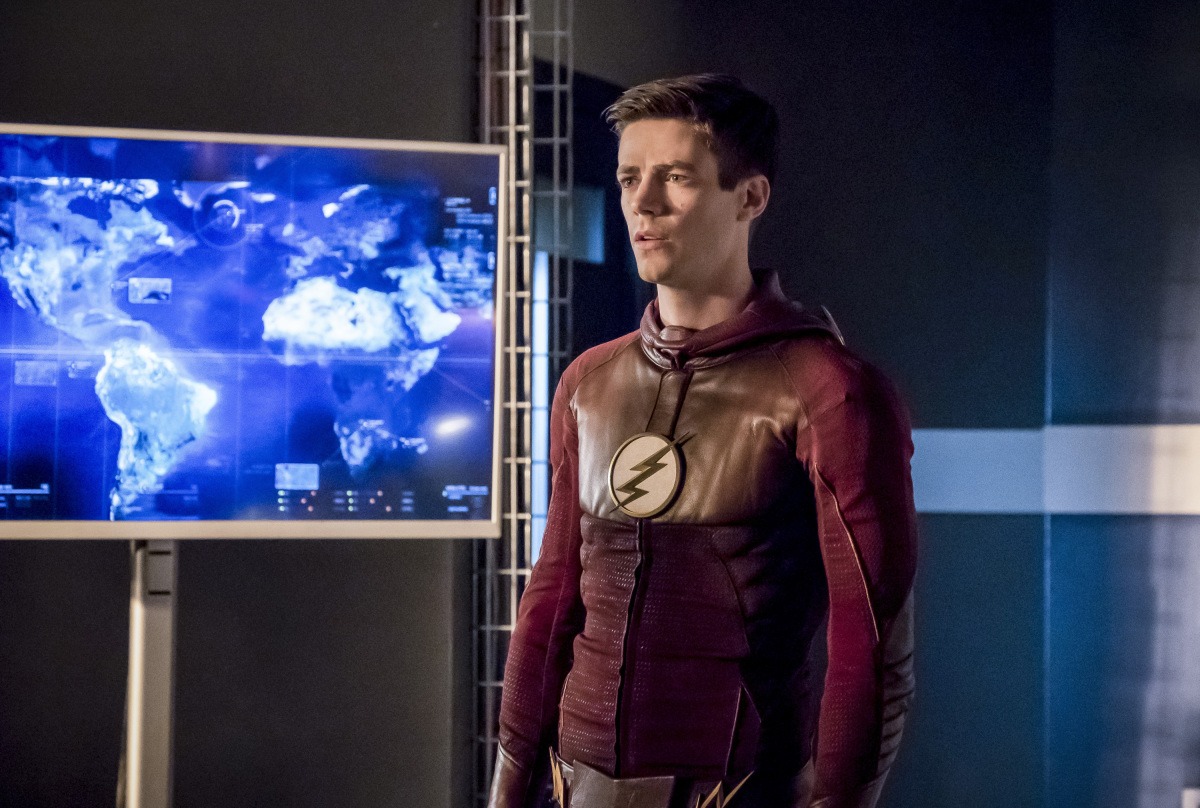 Grant Gustin wears his Flash costume in front of a blue map of the world in The Flash Season 3 finale