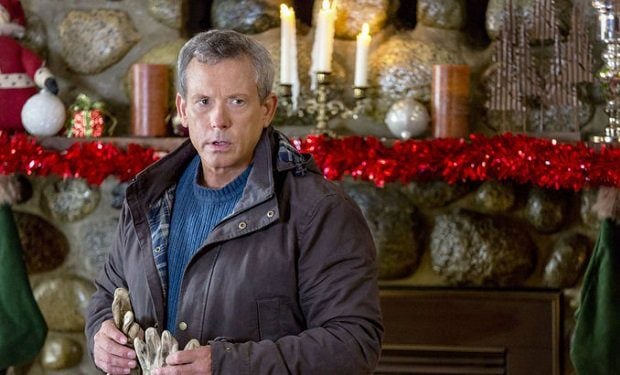Williw Aames as Vernon in front of a mantle decorated for Christmas