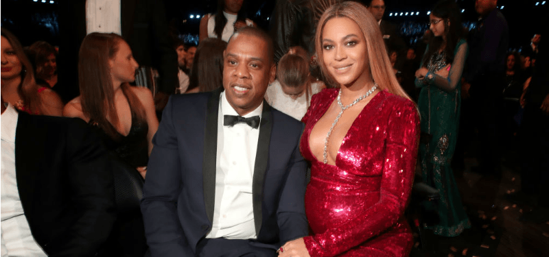 Beyoncé is wearing a red dress next to Jay Z in a tux.
