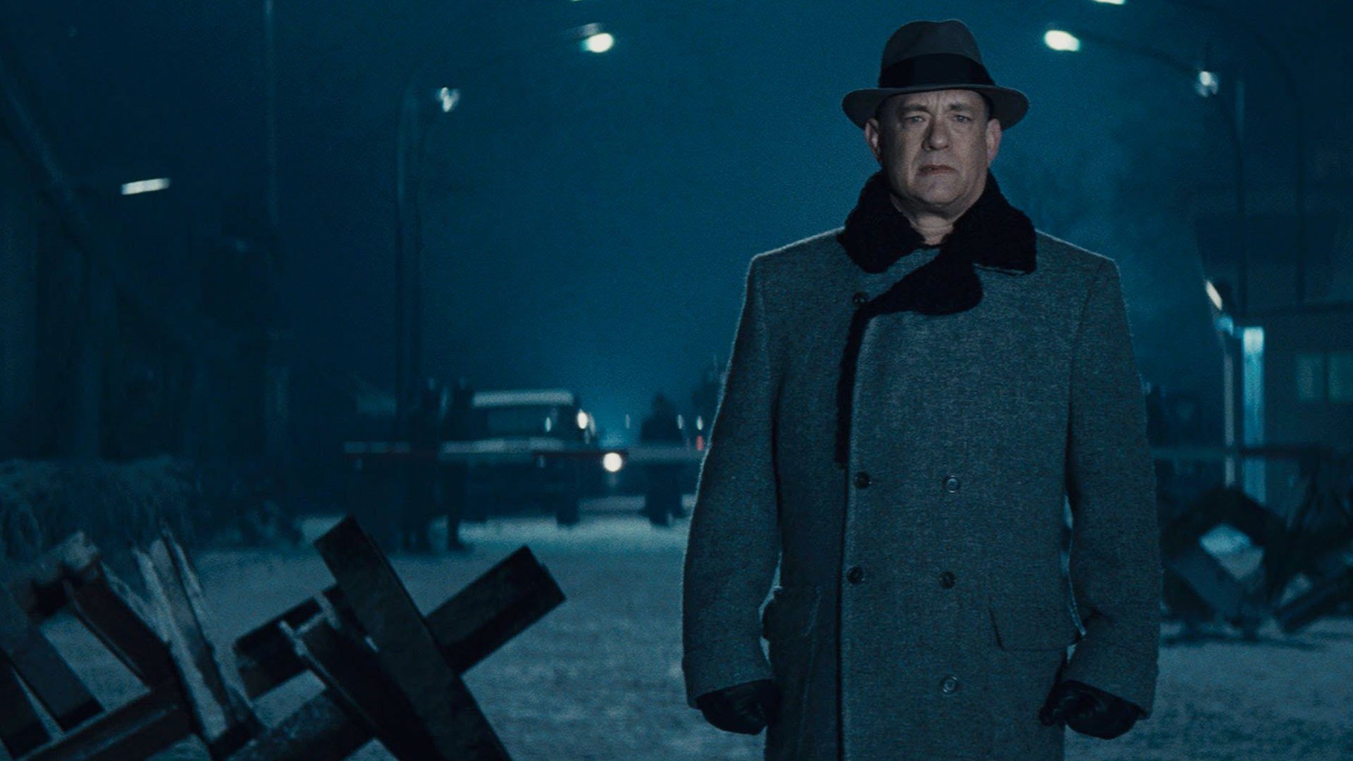 Tom Hanks stands in an empty street wearing a coat and a fedora in Bridge of Spies