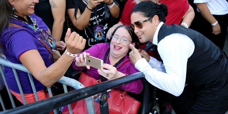 Chris Perez is bending down posing with a fan for a selfie.