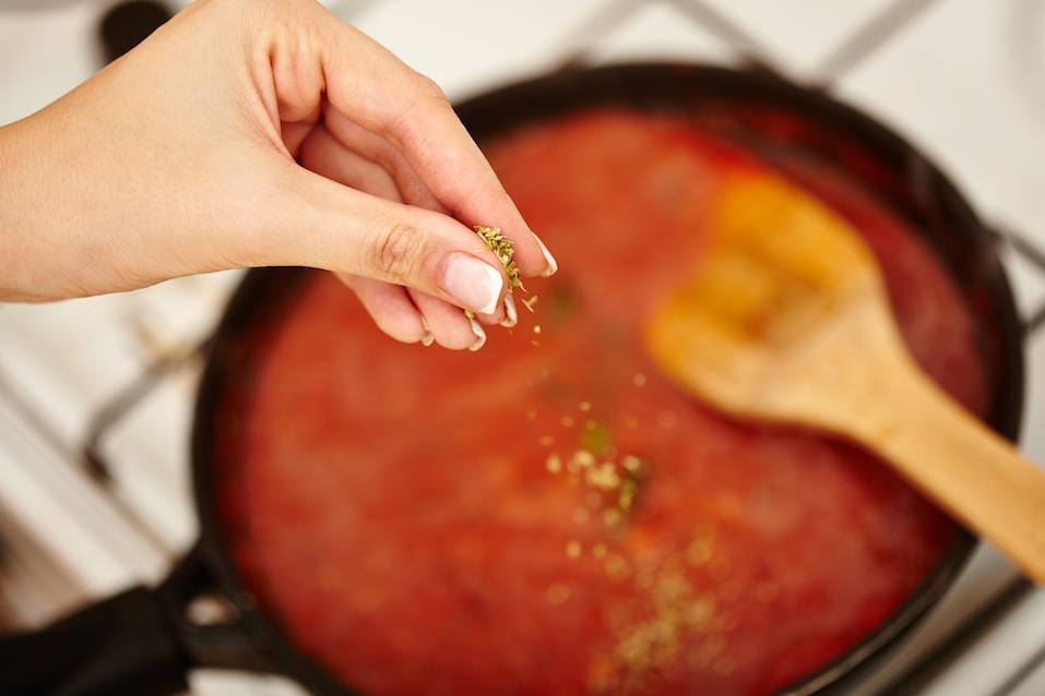 Closeup cook's hand sprinkling chopped parsley and basil in the tomato sauce pan on the stove