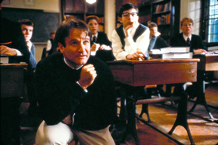 Robin Williams, crouched down in front of students sitting in a classroom