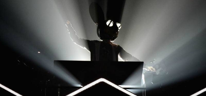 Deadmau5 is swinging his arms and is on a DJ booth.