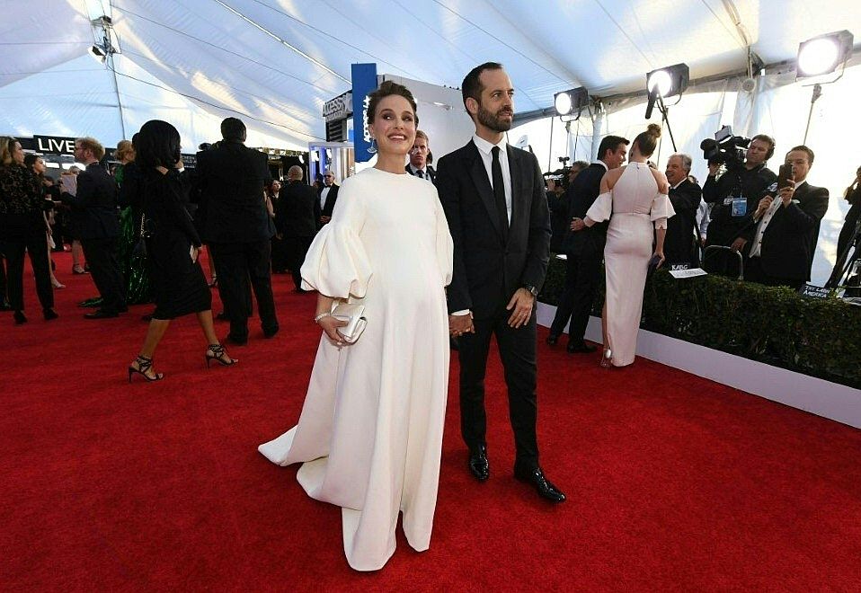Natalie Portman and Benjamin Millepied on the red carpet, posing for photos in a white dress and tuxedo respectively