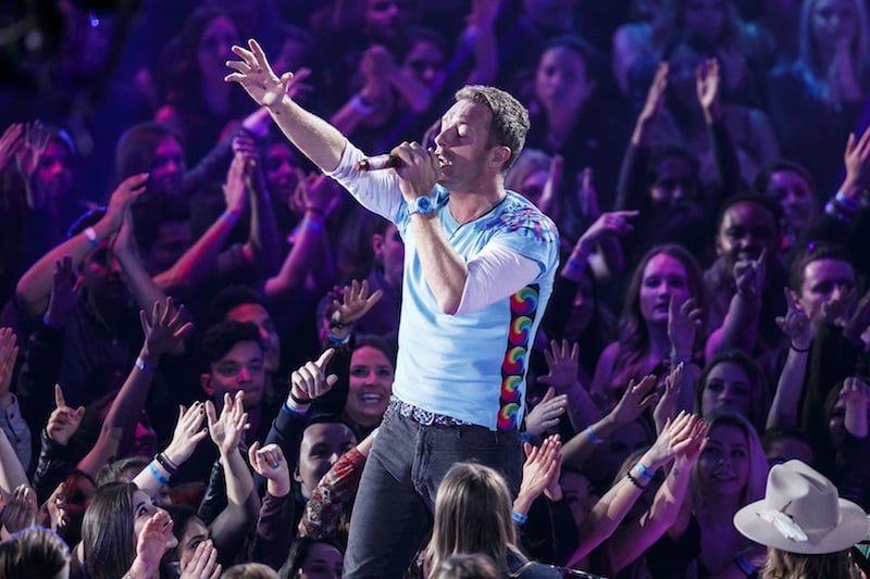 Singer-songwriter Chris Martin of Coldplay performs while fans reach up toward him