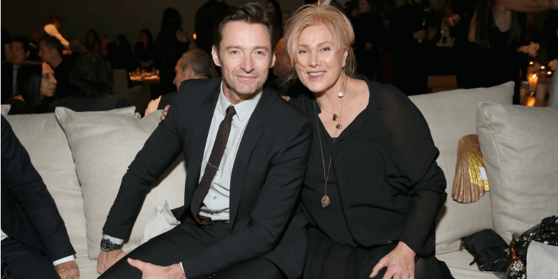 Hugh Jackman and Deborra-Lee Furness pose together sitting on a couch.