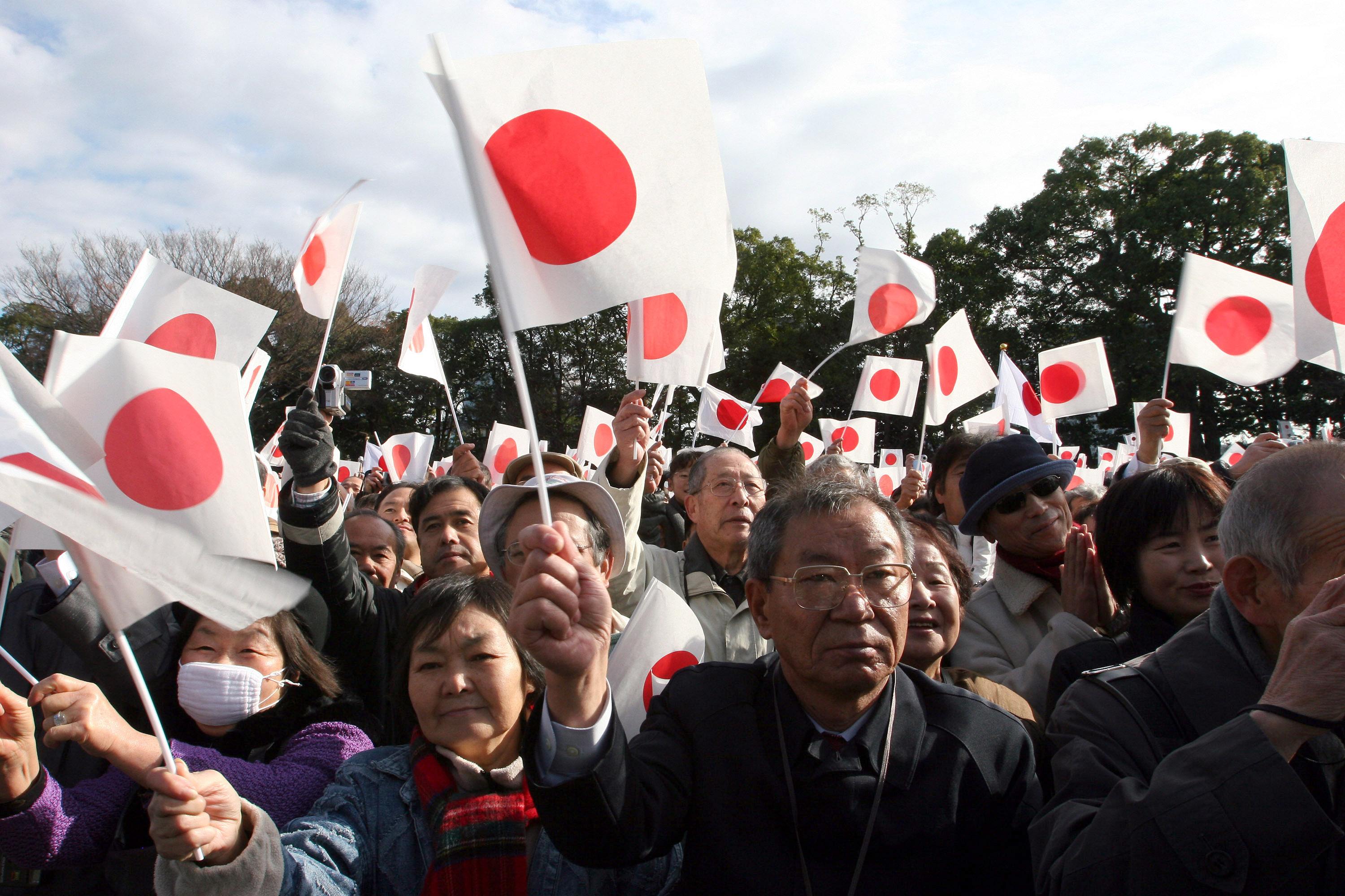 A crowd of people wave Japanese flags