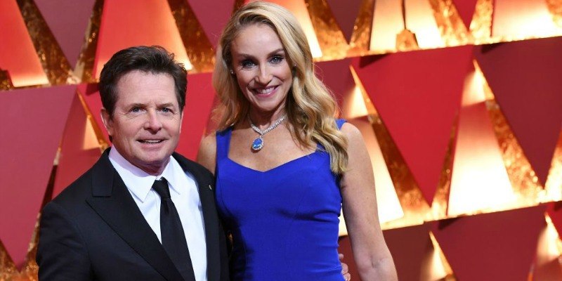Michael J. Fox is in a black suit and Tracy Pollan is in a blue dress on the red carpet.