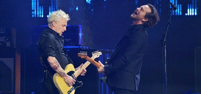 Mike McCready (L) and Eddie Vedder are playing guitar and bass facing each other on stage.