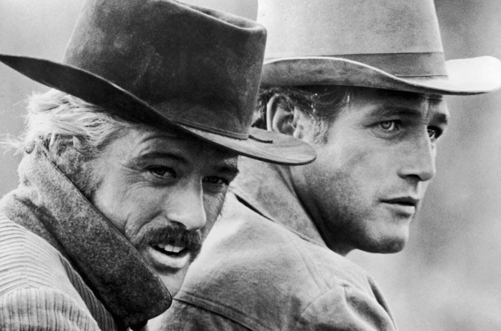 Robert Redford and Paul Newman in black and white, wearing cowboy hats and looking off to the right of the frame