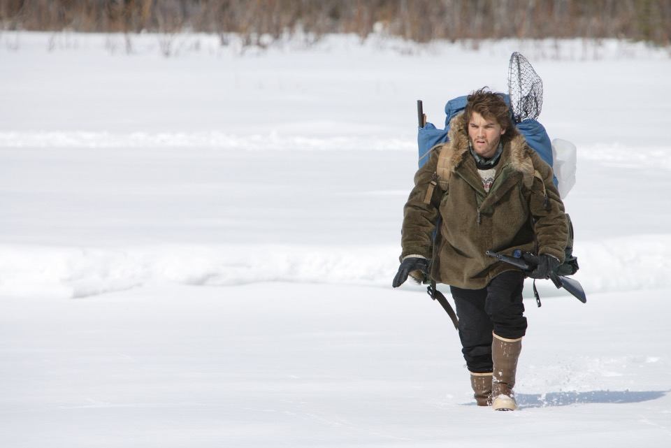 Emile Hirsch, wearing a coat and hiking backpack, trudging through the Alaskan snow