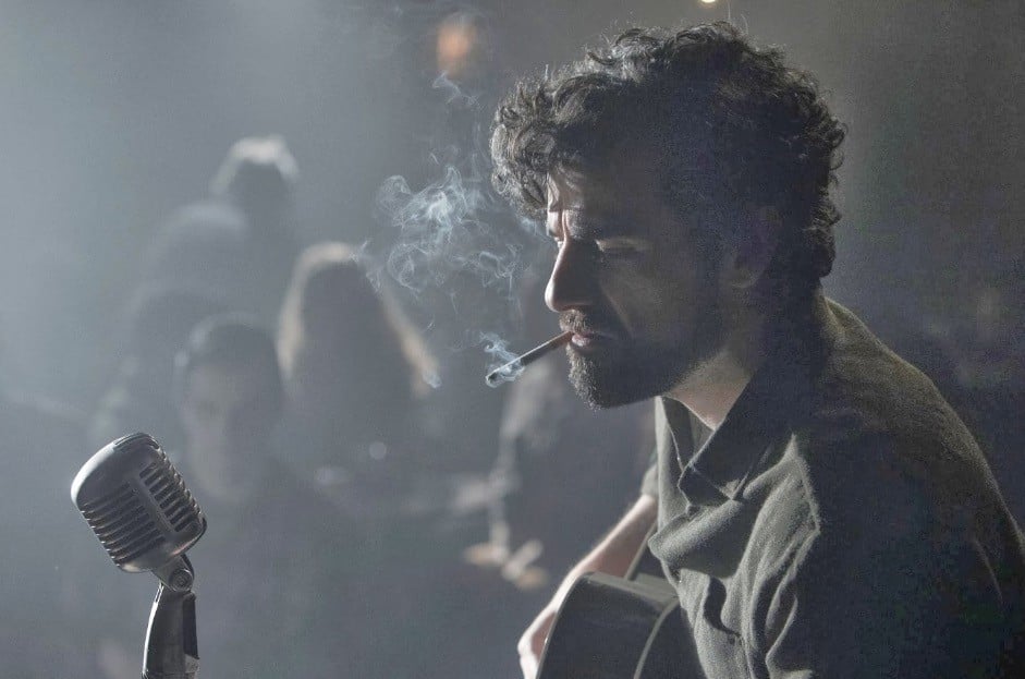 Oscar Isaac, smoking a cigarette on-stage, and playing a guitar