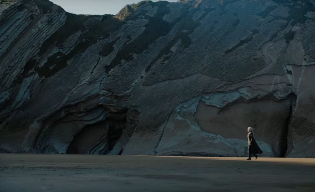 Daenerys Targaryen walking on a beach, with a tall mountainous ridge behind her