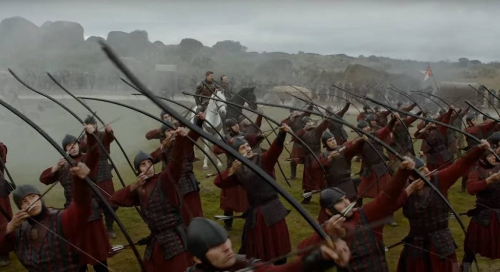 Jaime Lannister sitting on a horse behind a group of archers, who are all aiming their bows upwards