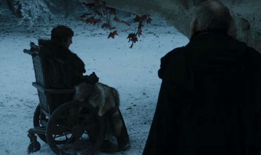 Bran, sitting in a wheelchair while an old man stands with his back to the camera next to him
