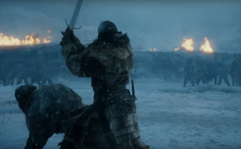 Jon Snow holding his sword over his head, as he brings it down on a man crouched on the ground in the snow