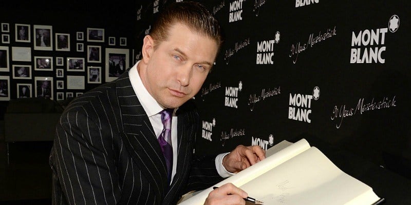 Stphen Baldwin is leaning over a book and is about to write.