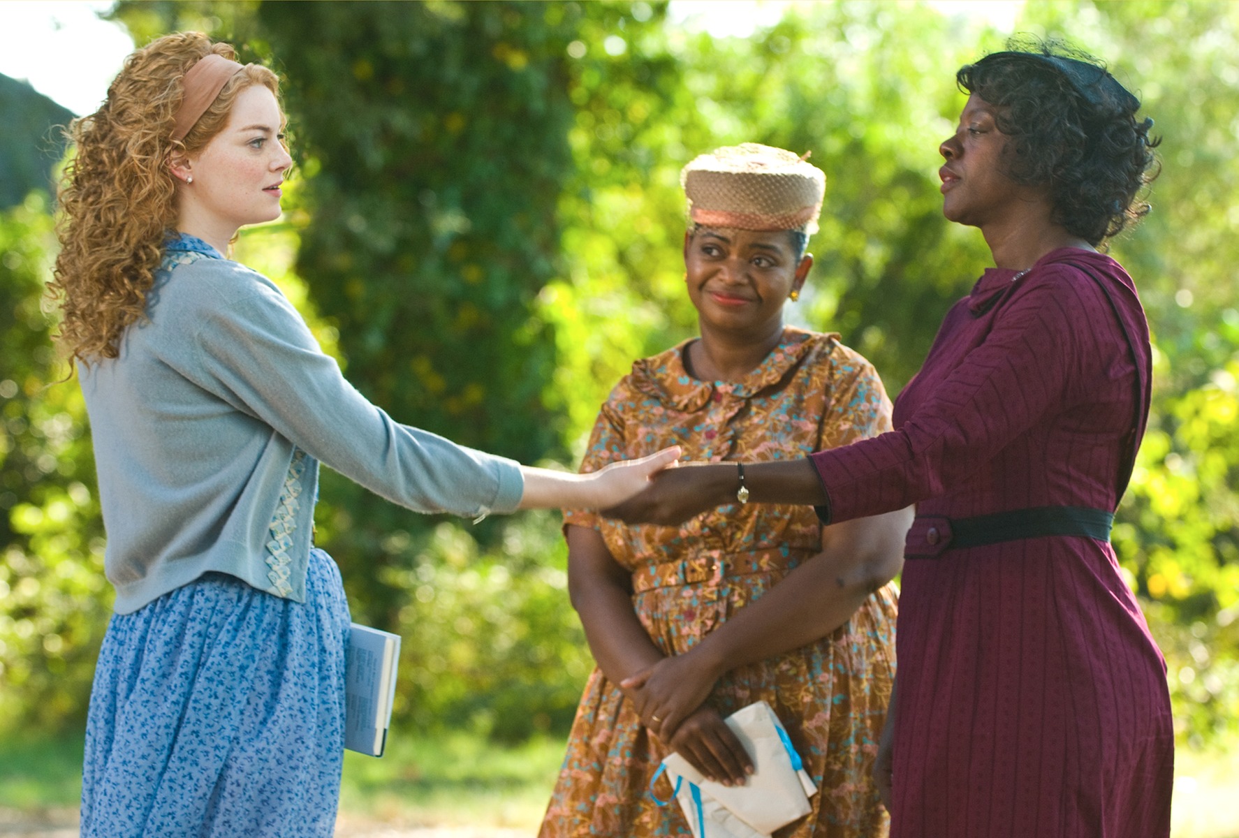 Viola Davis and Emma Stone, holding both hands together, while Octavia Spencer smiles in the background