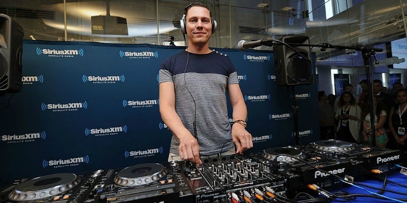 Tiesto is work on a sound board and smiling at the camera.
