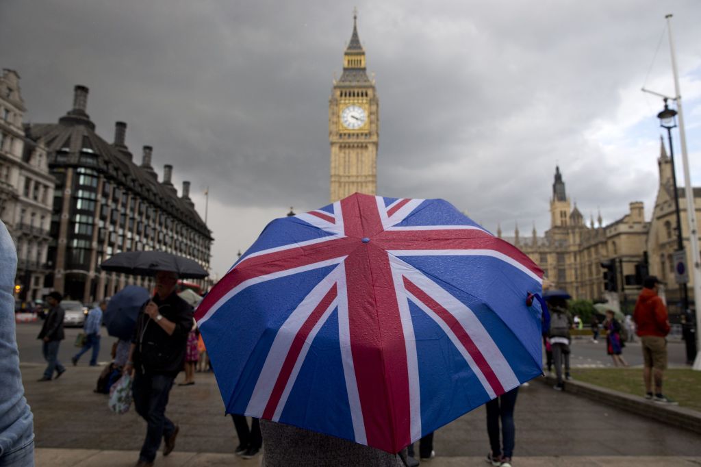 A pedestrian shelters from the rain beneath a Union Jack-themed umbrella.