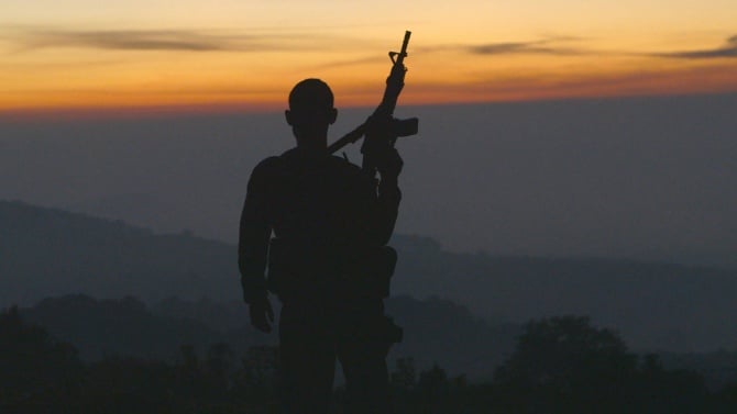 The silhouette of a man holding up a rifle while looking at a sunset
