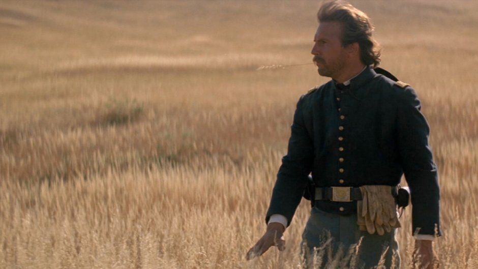 Kevin Costner dressed in a military uniform, walking through a grassy meadow
