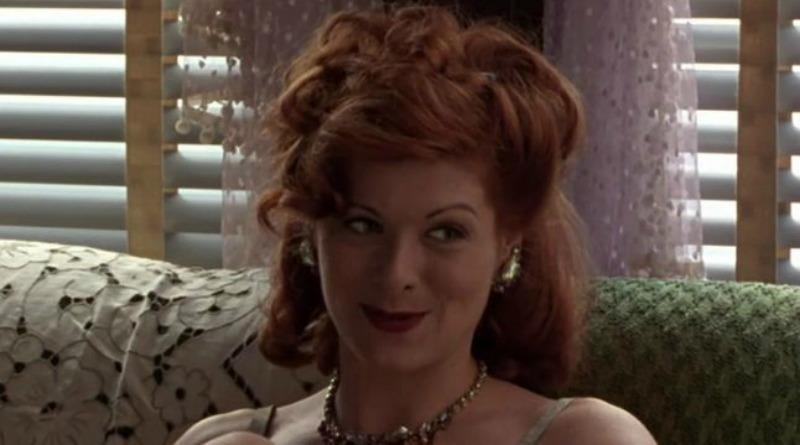 Debra Messing is smiling while sitting on a couch.