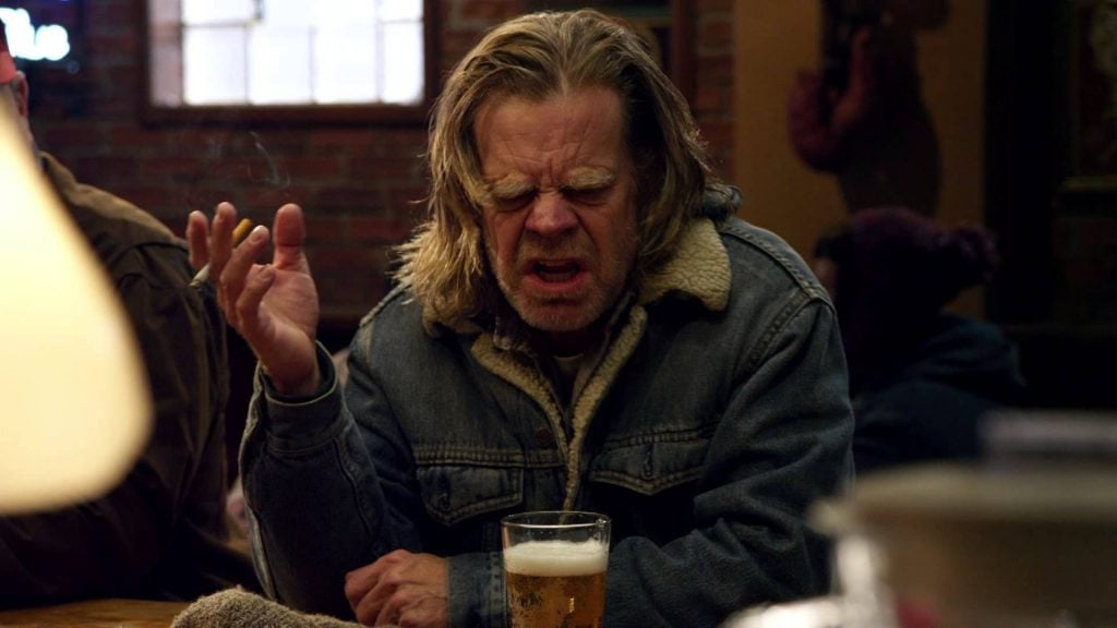 Frank Gallagher, with a cigarette in his right hand, and a beer in front of him, ranting angrily at a bar