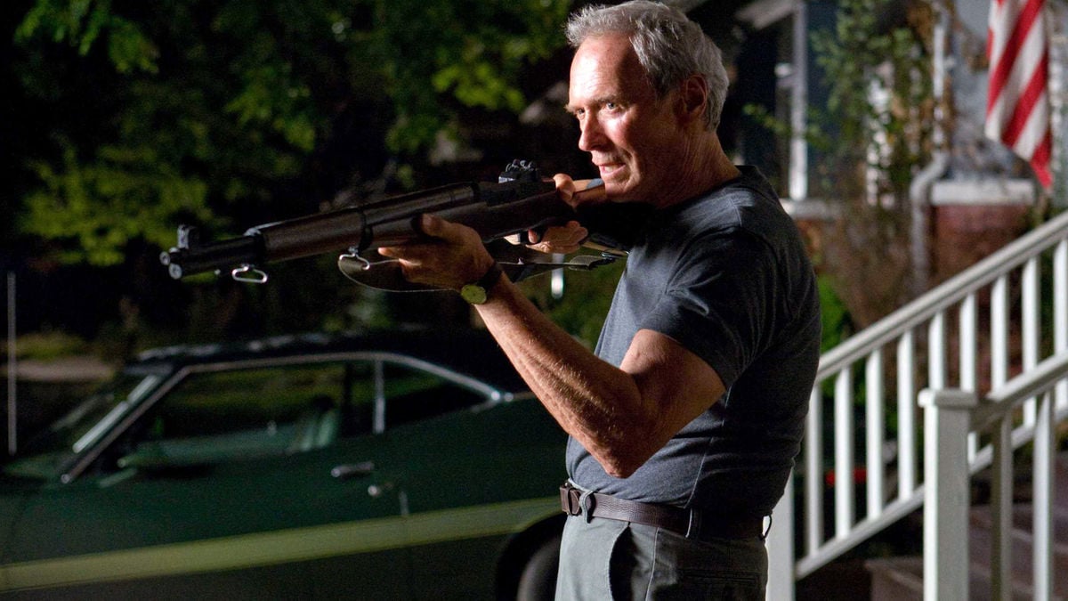Clint Eastwood aims a shotgun, with late day sun cast across his face