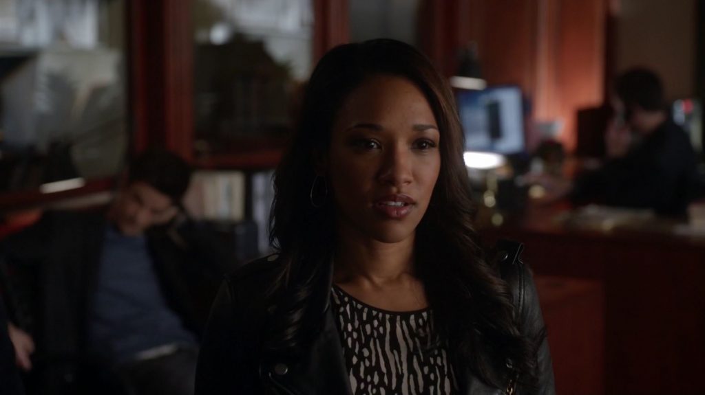 Iris West wearing a black leather jacket, with her mouth slightly open and looking off to the right of the frame