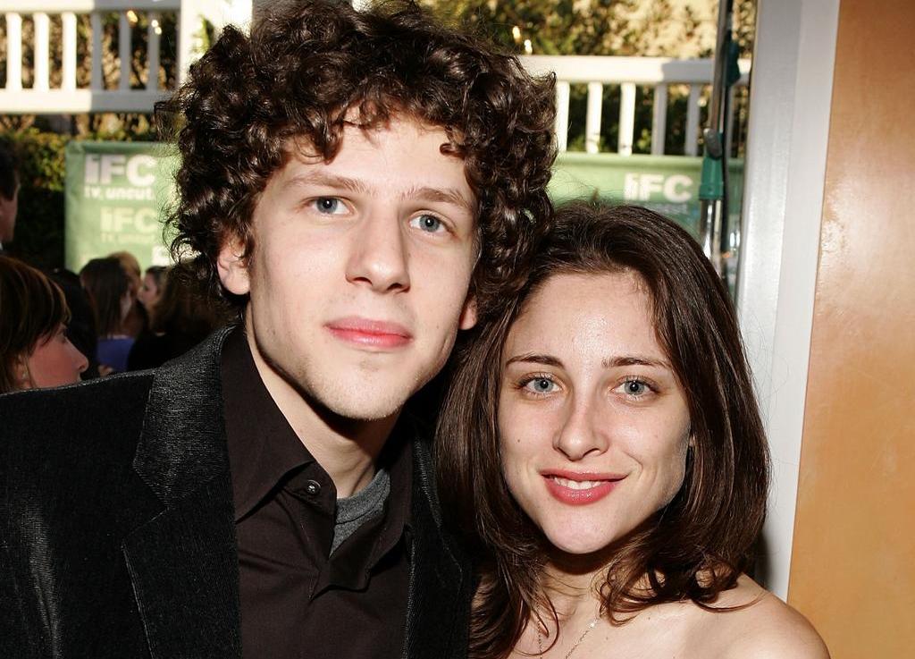 Jesse Eisenberg wearing a black velvet jacket, smiling for the camera with girlfriend Anna Strout