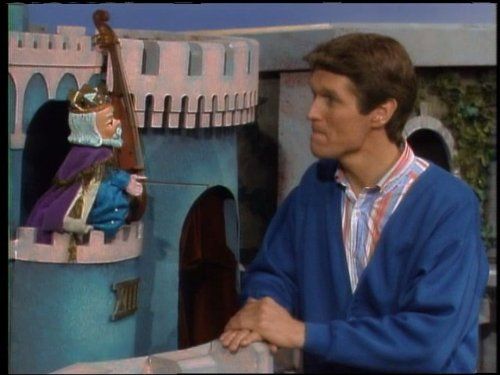 A king puppet in a castle speaking to a human man