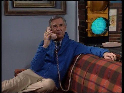 Fred Rogers sitting on a couch talking on the phone in front of a traffic light shining green